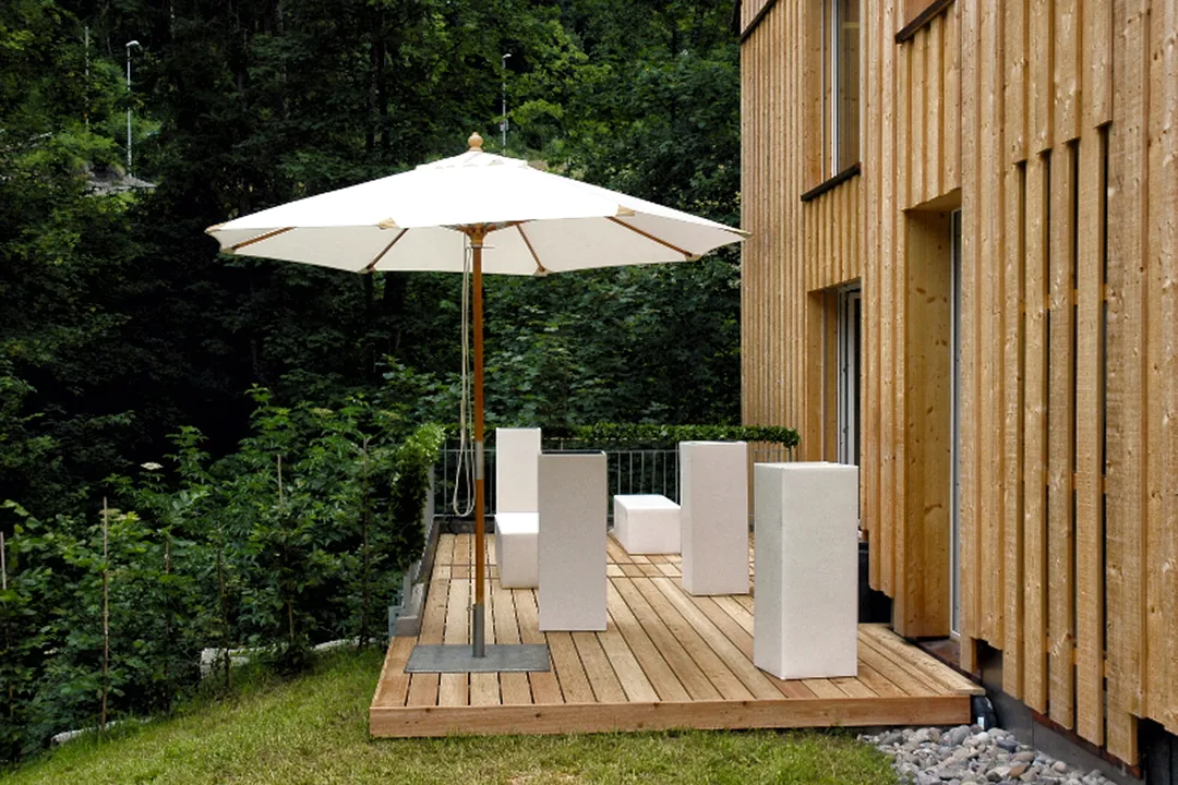 Flow60 terrace — wooden deck with parasol surrounded by lush greenery and forest