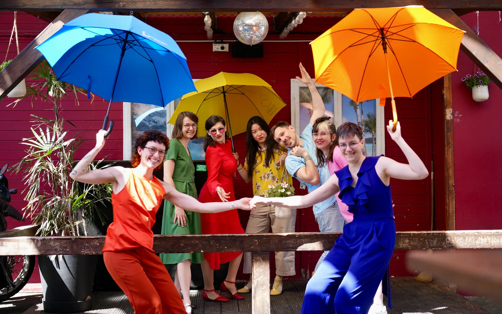 QSXZ team in expressive dance-like poses with rainbow umbrellas